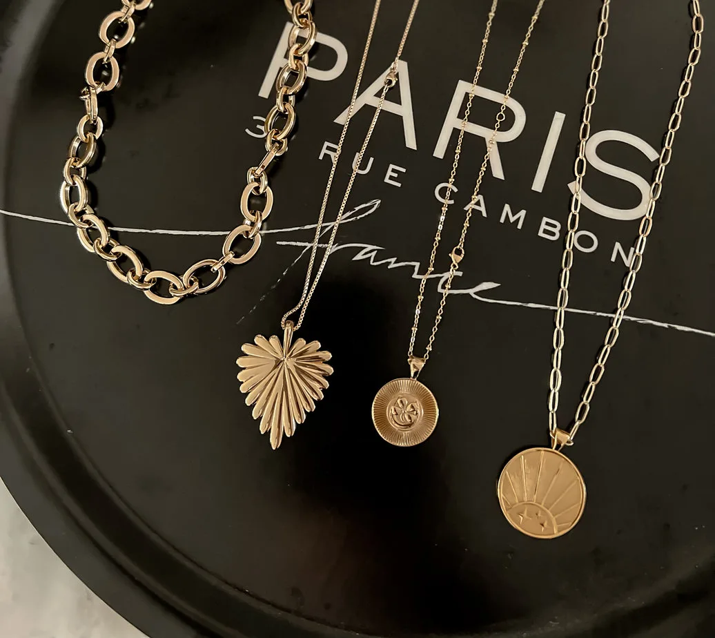 4 gold necklaces for layering on top of a black tray that says Paris