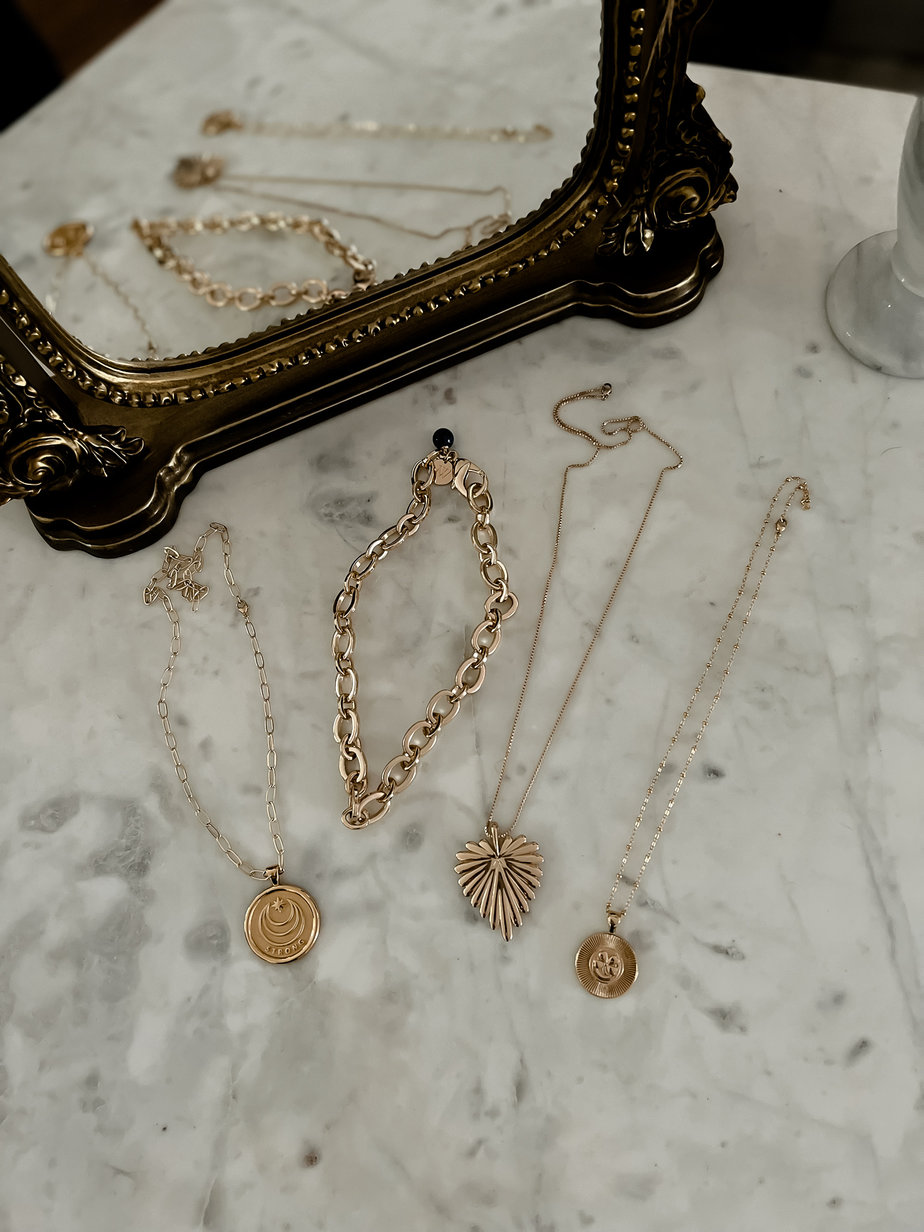 4 Gold necklaces to layer sitting on a marble table