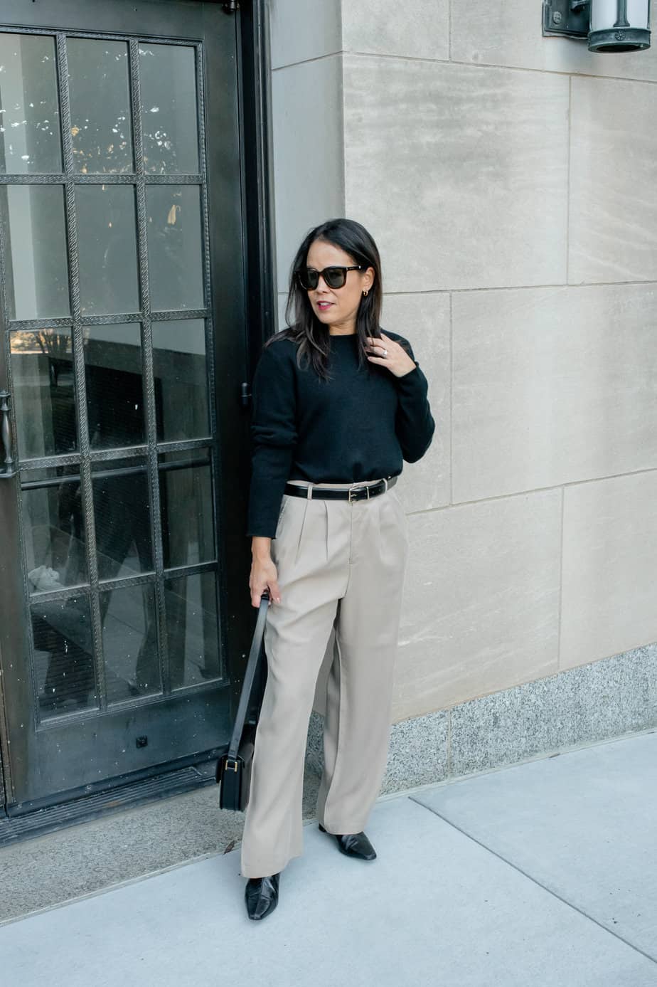 Woman wearing black sweater with trousers, glassed and black handbag.