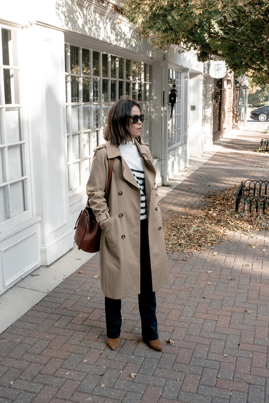 woman wearing trench coat with brown boots, brown leather bag, and striped sweater showing sezane fall pieces.
