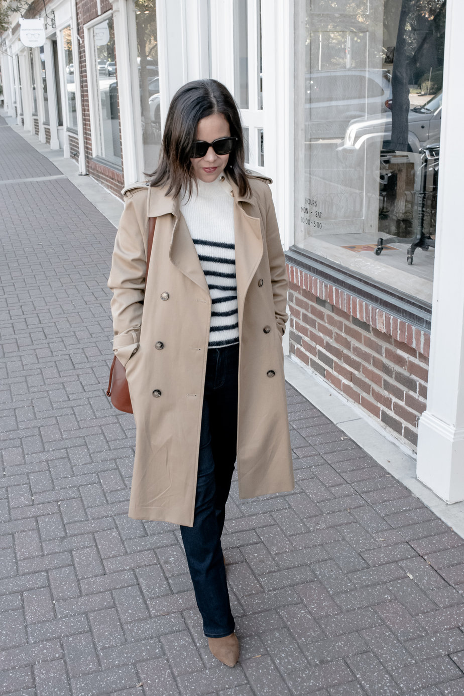 Woman wearing trench coat with striped sweater, jeans, and boots.