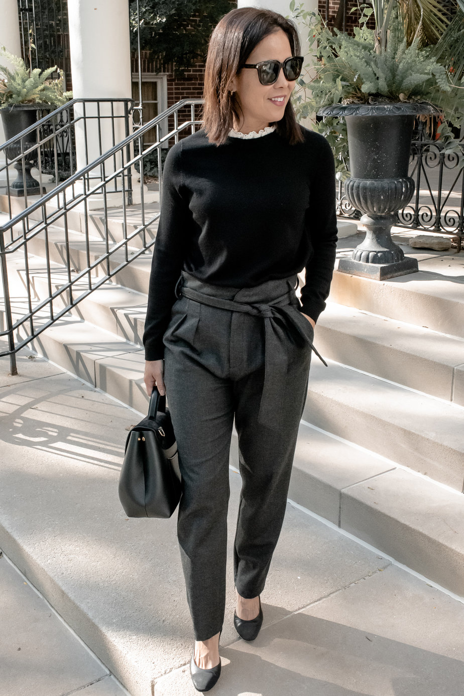 Girl wearing grey pants with black sweater and black slingbacks and black leather bag, which is a sezane fall favorite.