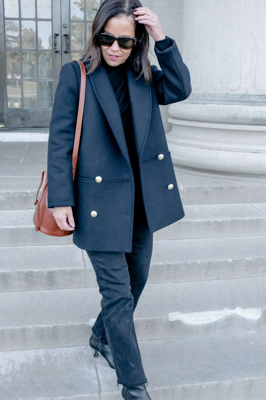 Lady walking down the stairs wearing navy jacket with gold buttons, black denim, and brown handbag of sezane fall favorites