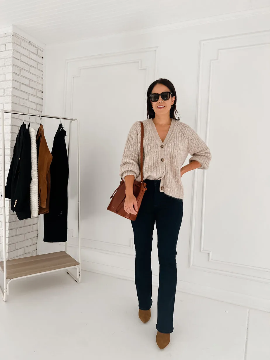 Wearing sezane cardigan, blue denim, brown boots, bucket bag, and sunglasses against a white wall
