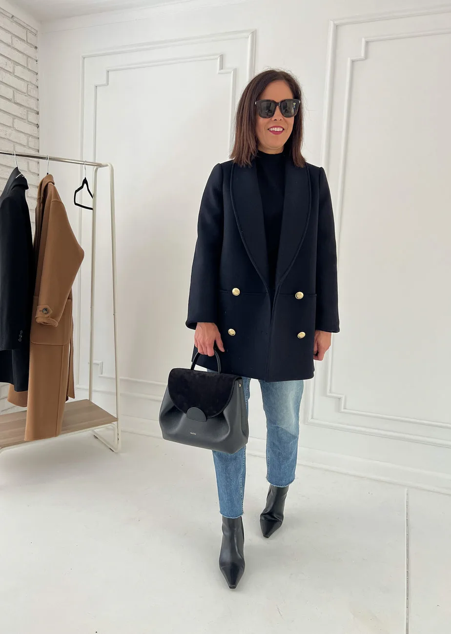 wearing navy jacket with black turtleneck, boots, denim, and carrying black bag
