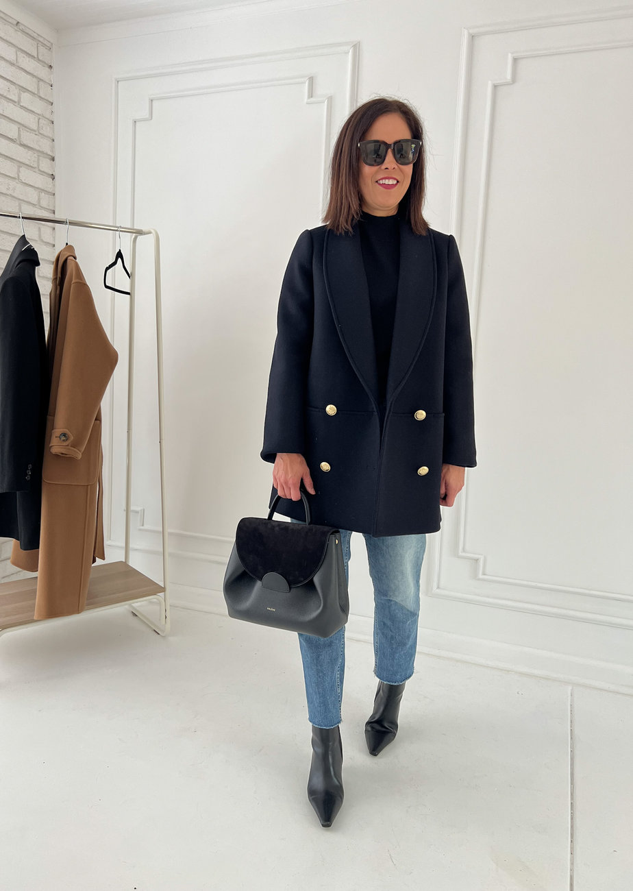 wearing navy jacket with black turtleneck, boots, denim, and carrying black bag