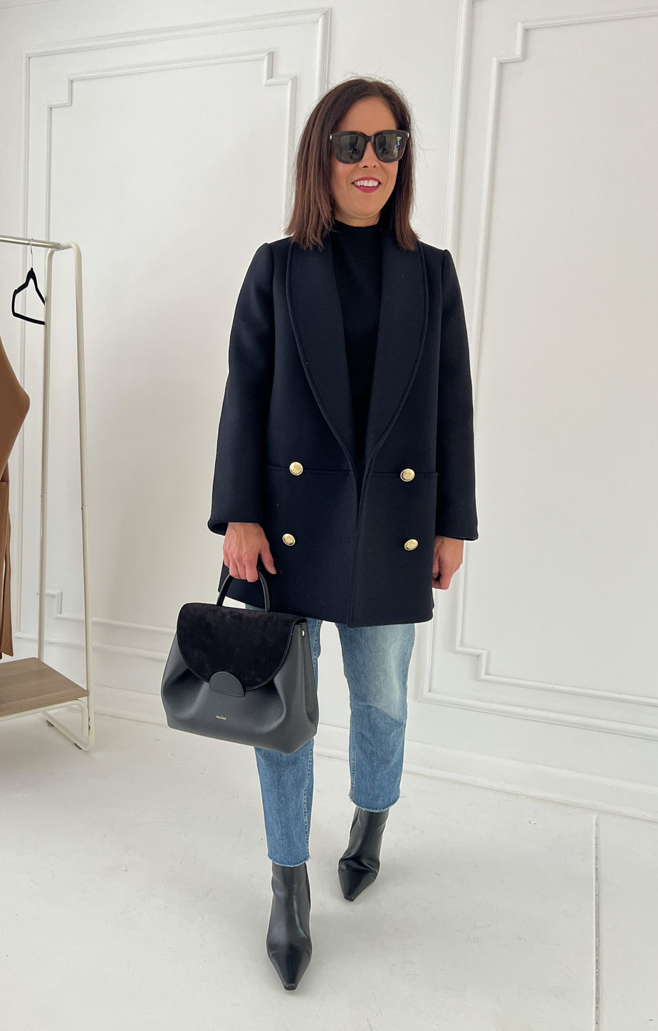 wearing navy jacket with black turtleneck, boots, denim, and carrying black bag