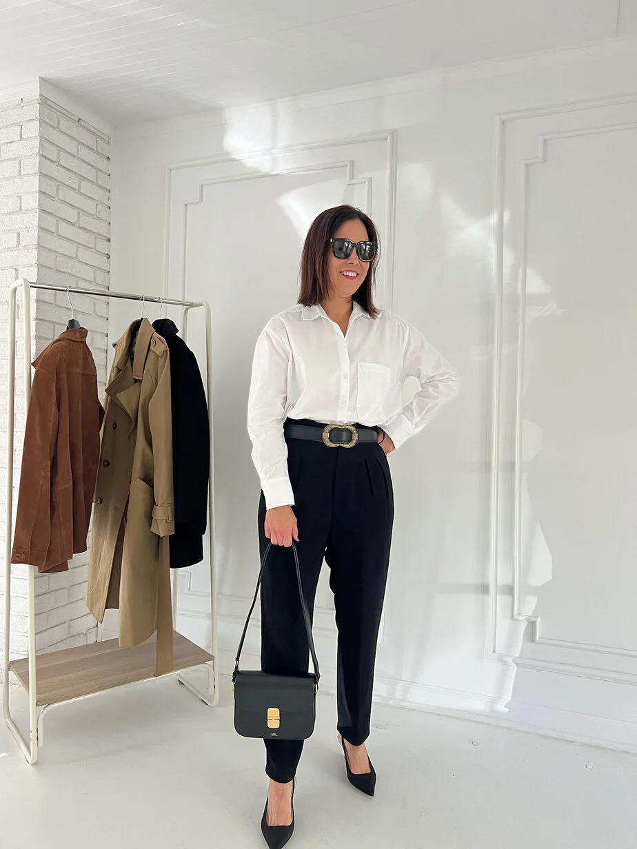 Lady wearing white button down, black pants, leather handbag, belt and slingbacks.