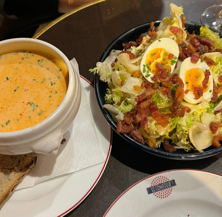Bowl of soup and a salad sitting on a table with a bowl that says Comptoir.