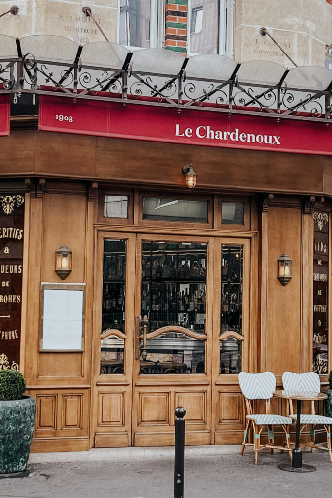 Outside exterior of Le Chardenoux in Paris with a red awning and wood panels.