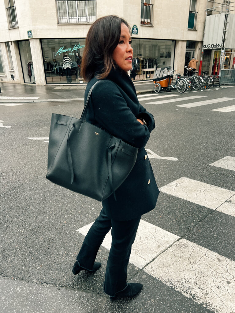 Standing on Parisian street with black handbag, navy coat, black denim, and boots.