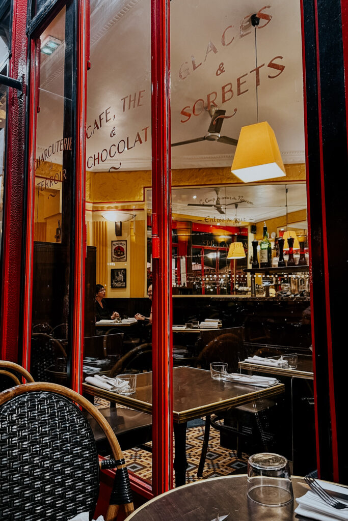 Le Comptoir Exterior in paris looking from outside into the inside. Cafe black chairs and red exteiror.