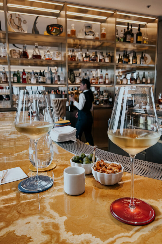 Two wine glasses sitting on a bar table with server in the background.