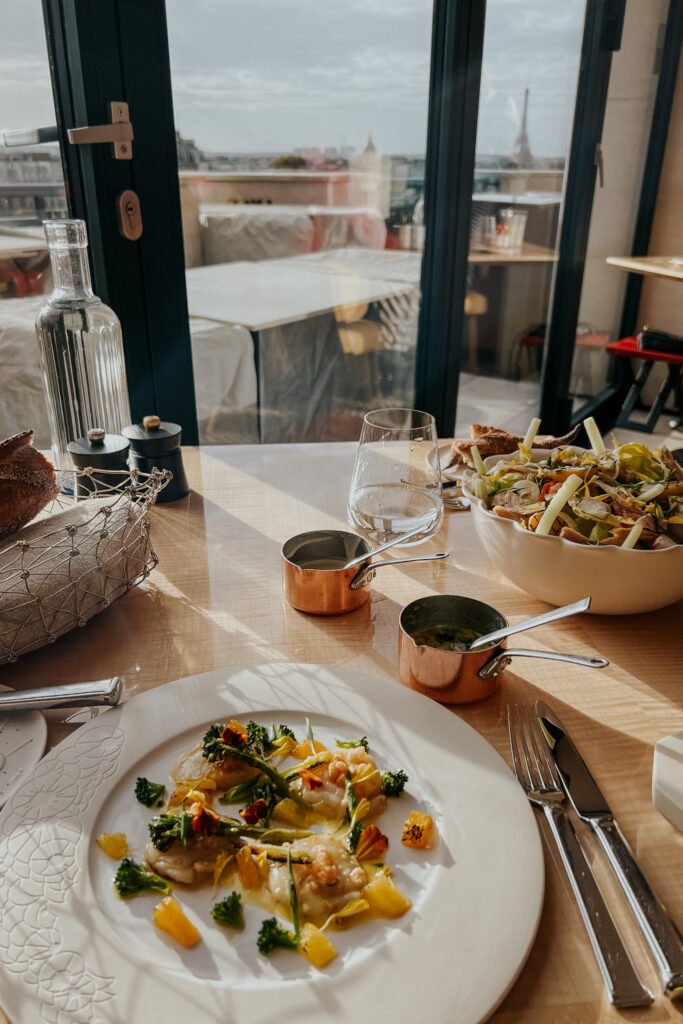 Scallops on a plate and a salad in a bowl sitting on a table with eiffel tower in the background in Paris.