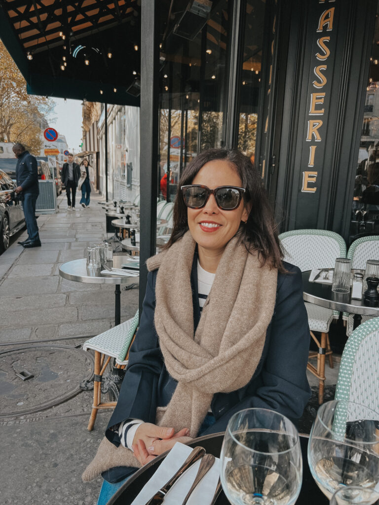 Sitting at a cafe wearing camel scarf and navy blazer in Paris.