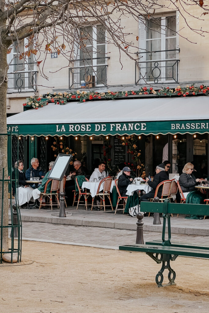 La Rose De France exterior. People sitting on a patio in Place Dauphine in where to eat in Paris.