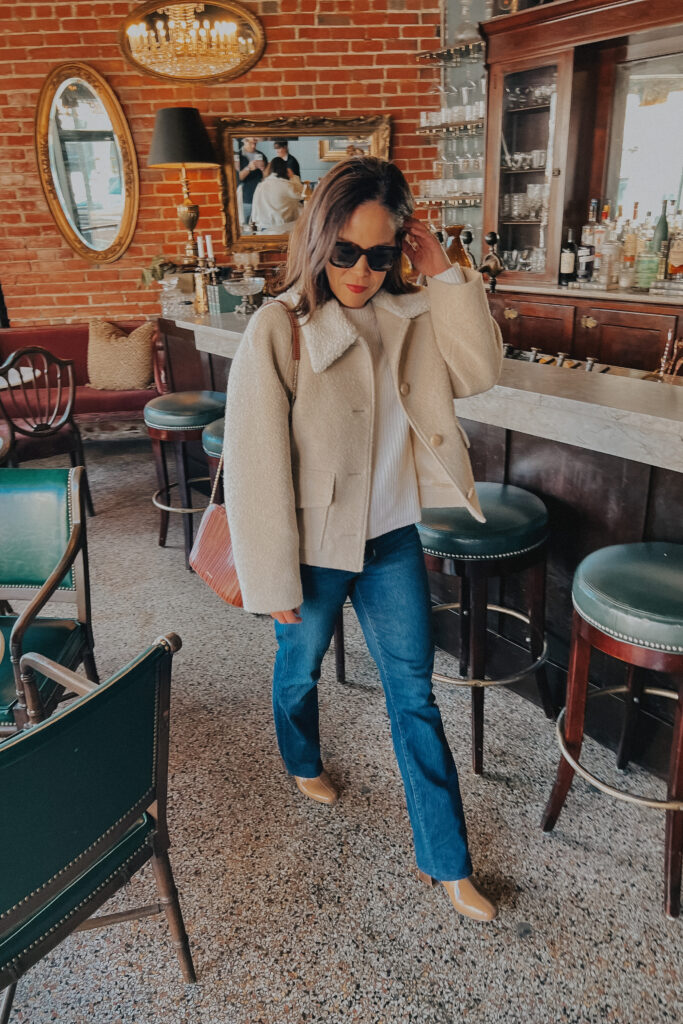 Woman wearing a boulce coat and jeans in a front of a bar.