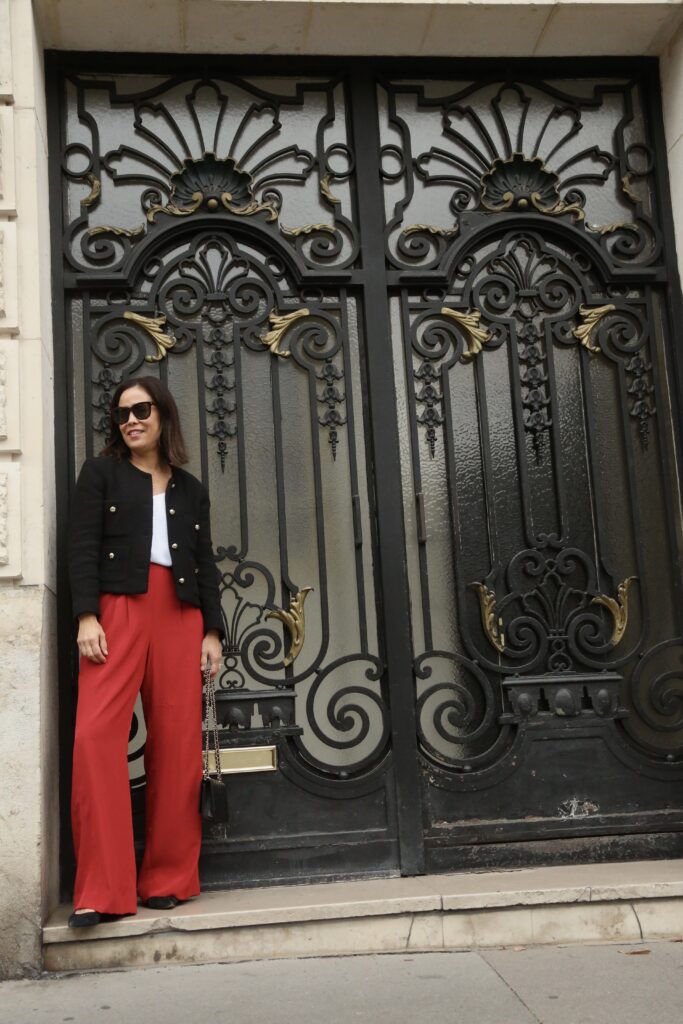 Woman standing in a doorway wearing red pants, black tweed blazer, and white cami.