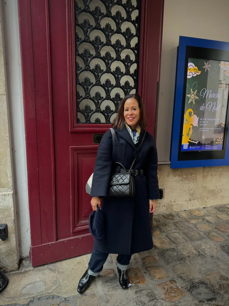 Women's navy trench coat standing in front of red door in Paris.