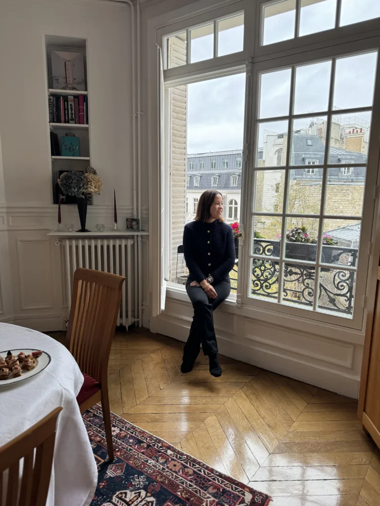 Lady looking out a big Parisian window.