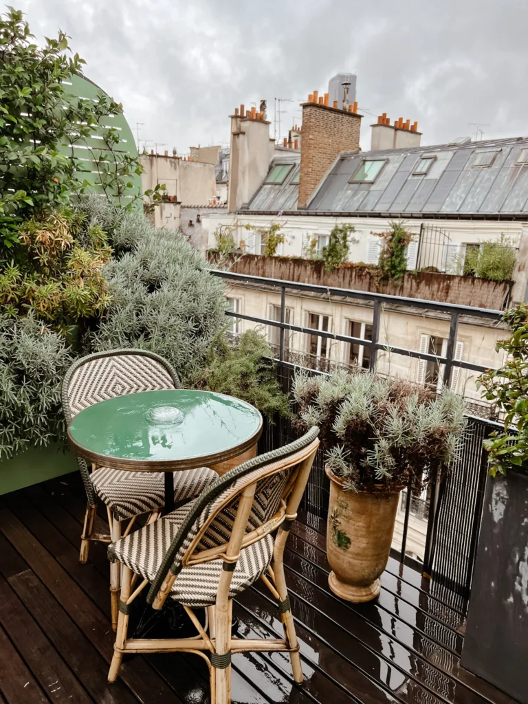 Two cafe chairs and a green table sitting on a terrace in paris.