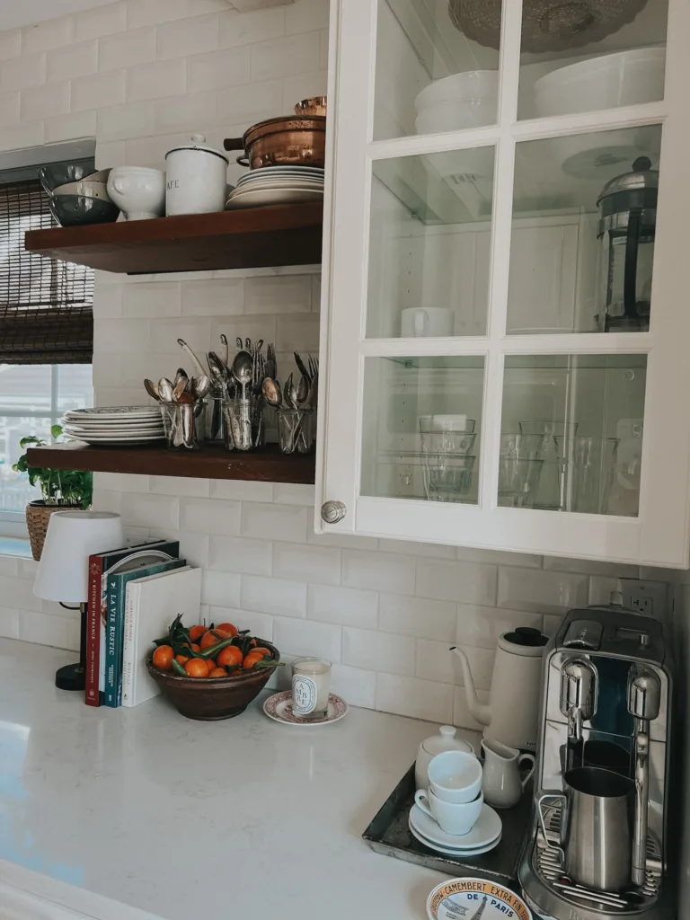 Nespresso maker in kitchen corner with 3 wood shelves and glass cabinet.