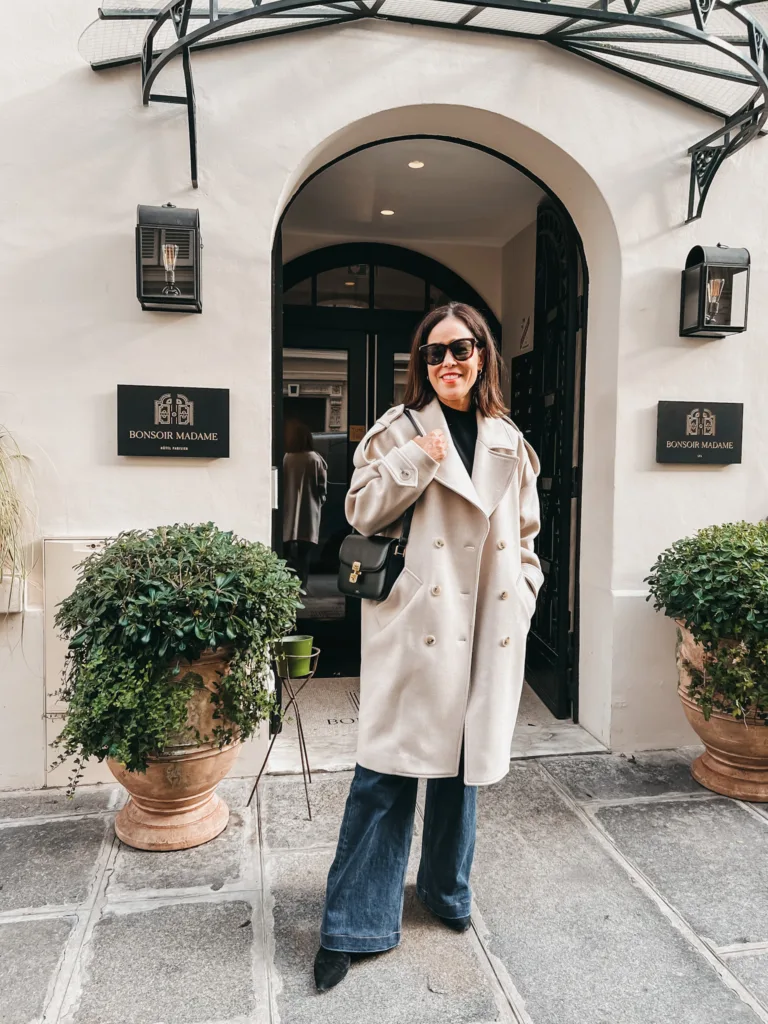 cream coat paris outfit Lady in cream coat standing outside hotel in Paris.