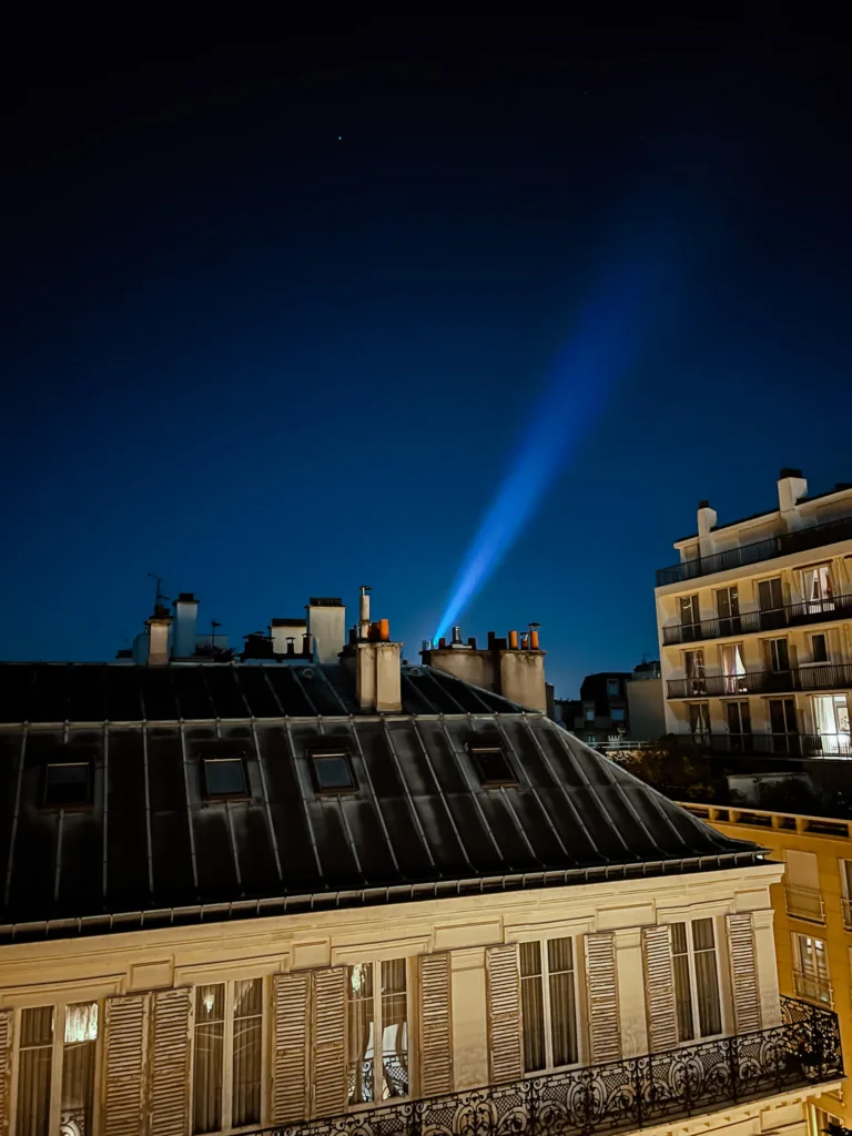 Beacon from eiffel tower shining through skyline at night in Paris.