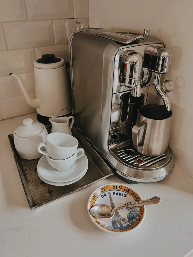 Nespresso machine in a corner with white espresso cups and frothing unit.