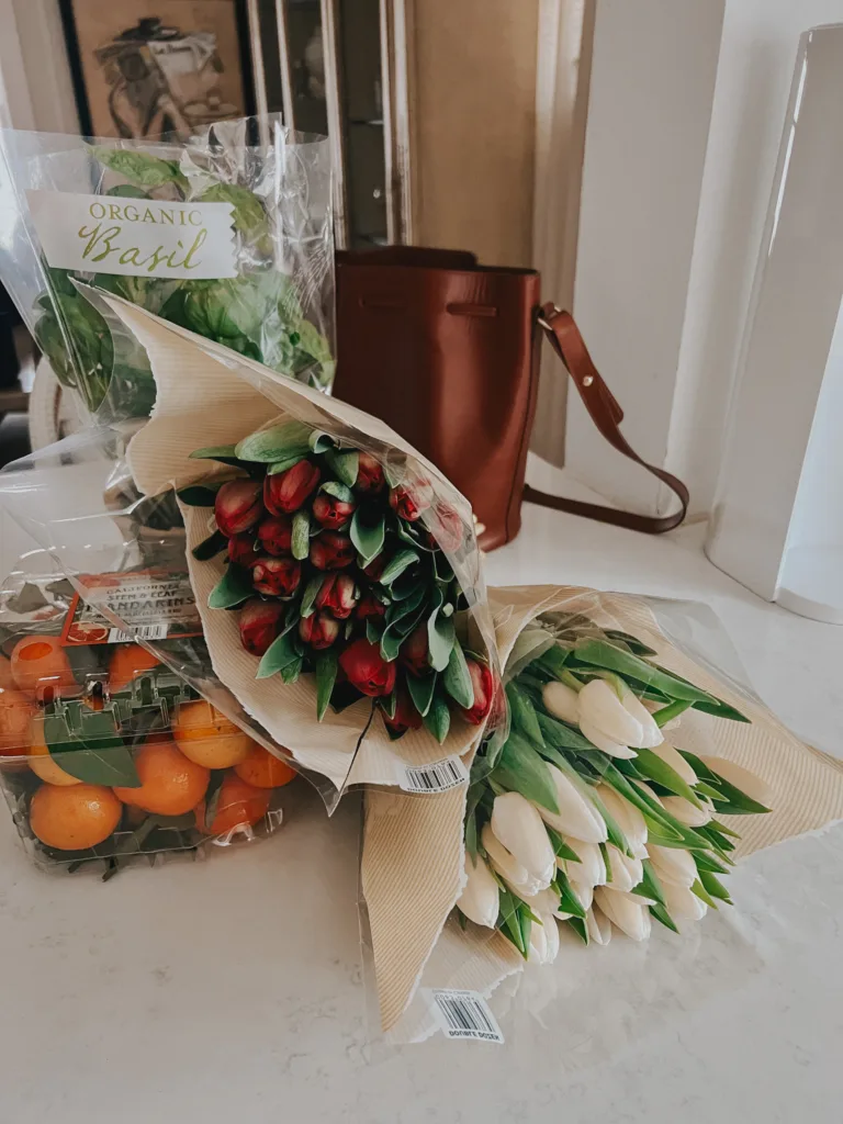 Tulips, oranges, and basil plant with a brown handbag sitting on kitchen counter.