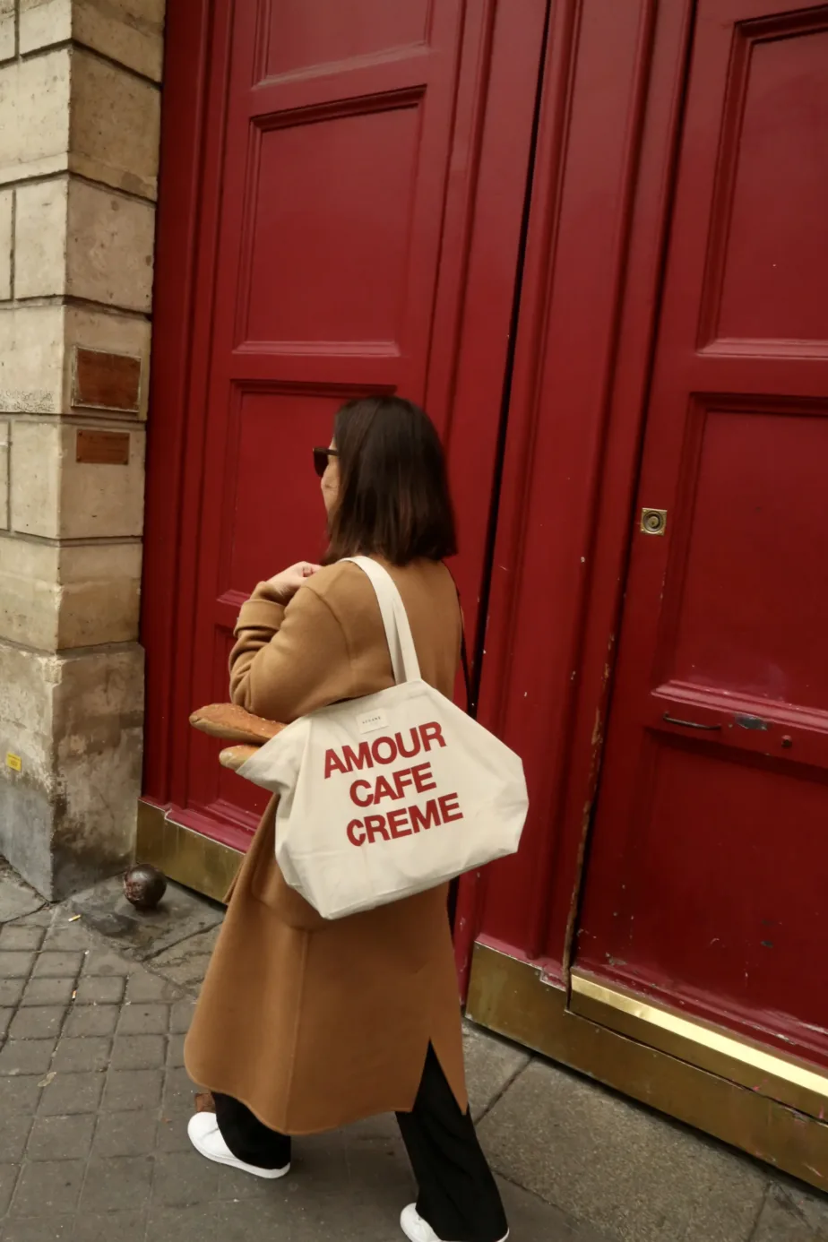 Lady wearing camel coat and carrying canvas bag that says Amour Cafe Creme.