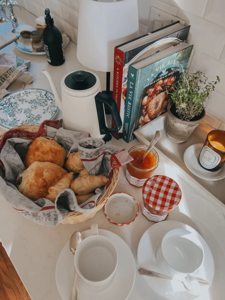 Kettle, jar of jame, croissants, cup and saucer on the counter.