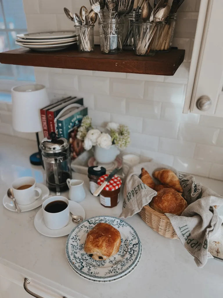 Sunday Mornings In Paris: Coffee in cup and saucer on the counter with croissants, jame, bread basket.