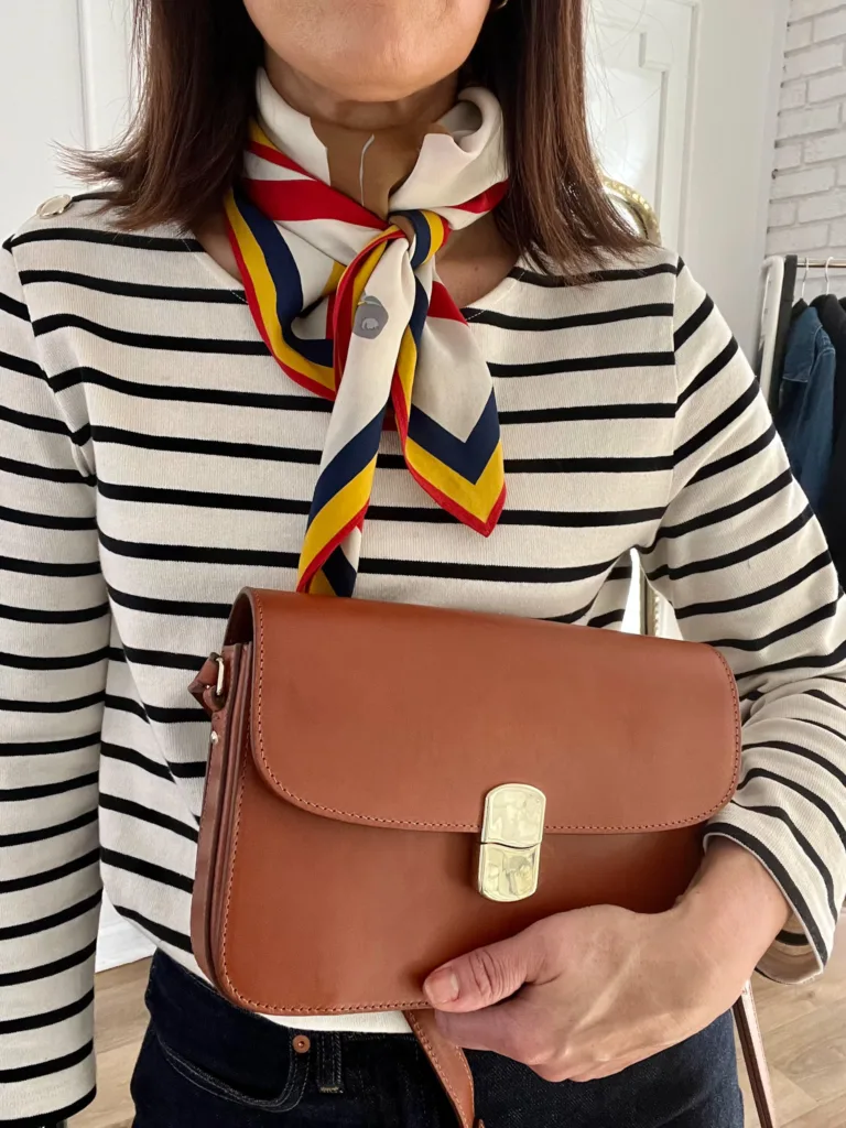 Women in striped shirt with scarf and holding brown handbag.