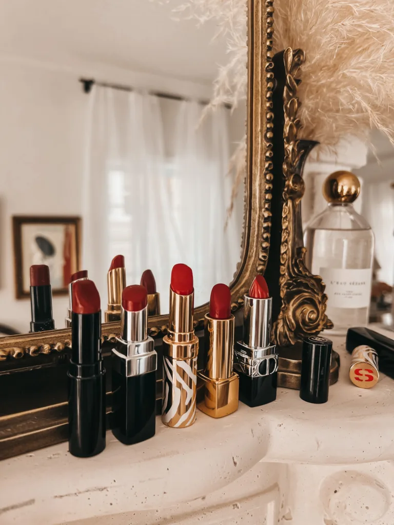 5 French red lipsticks sitting on a fireplace mantle with mirror in background.