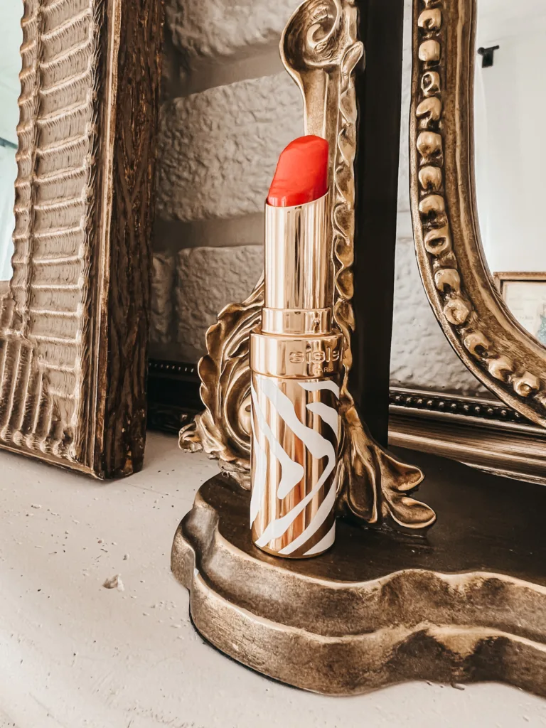 Sisley red lipstick sitting on top of a mantle with gold mirror in background.