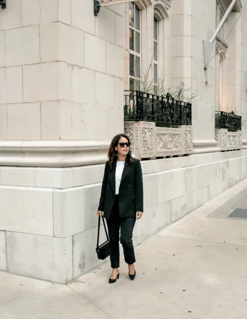 Woman wearing black jacket, black jeans, white tee, and black bag.