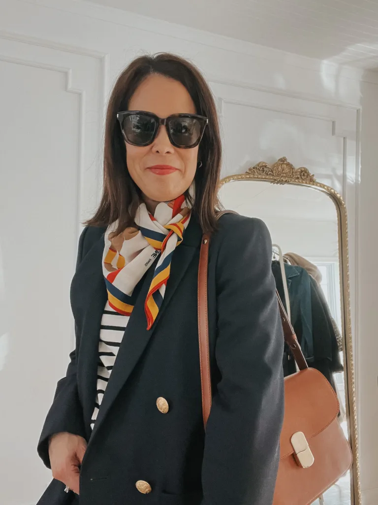 Woman wearing scarf with stripe top, navy blazer, and brown bag.