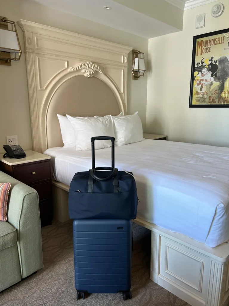 suitcase and bag sitting in a room next to a white bed at disneyworld.