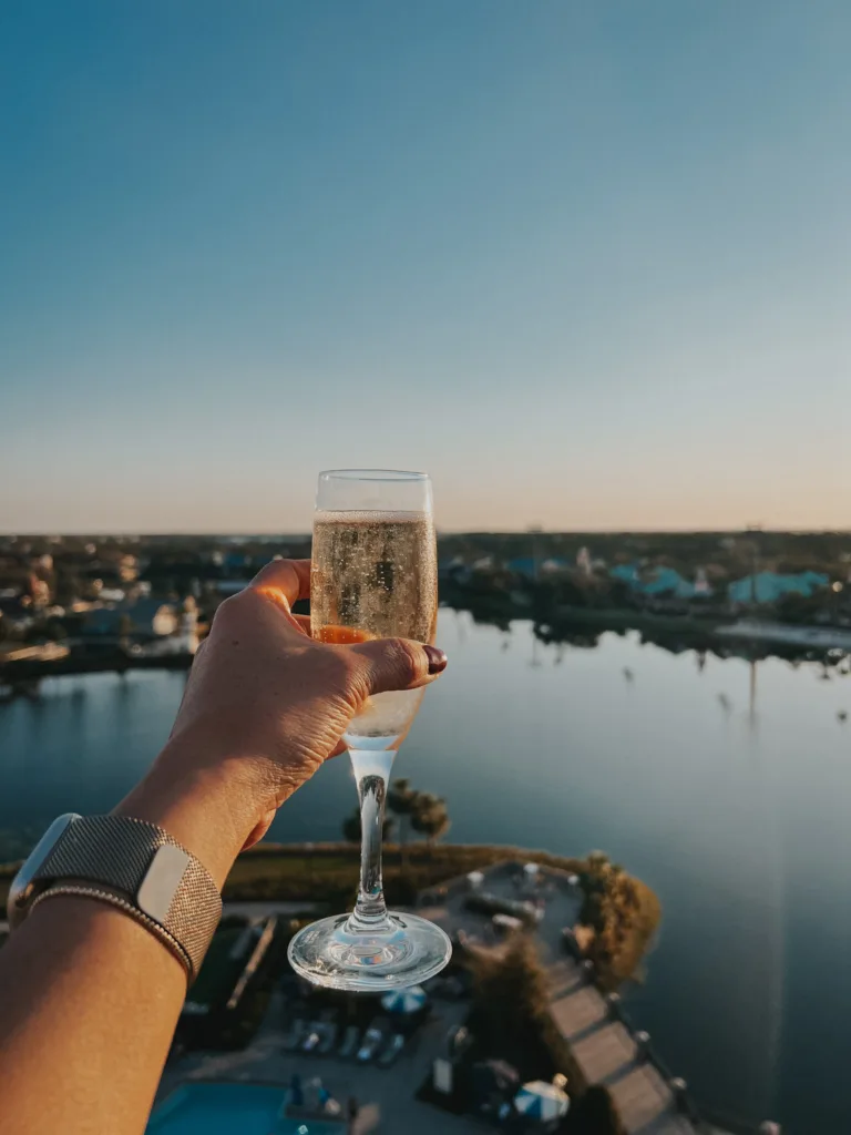 Holding a glass of champagne looking out at a lake at Disneyworld.