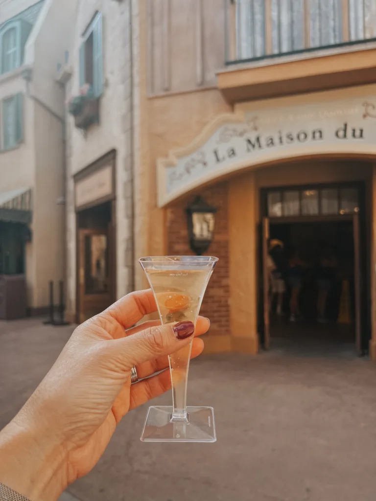 Woman holding glass of champagne in front of French store at Epcot, favorite french inspired things at Disneyworld.