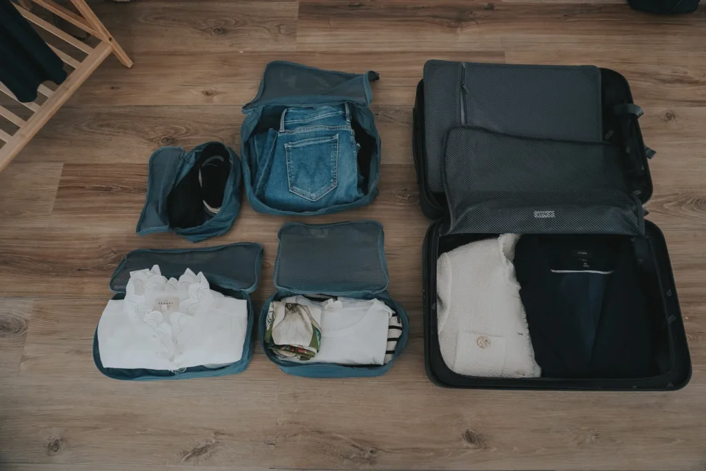 Packing cubes with clothes inside the cubes and a suitcase next to it.