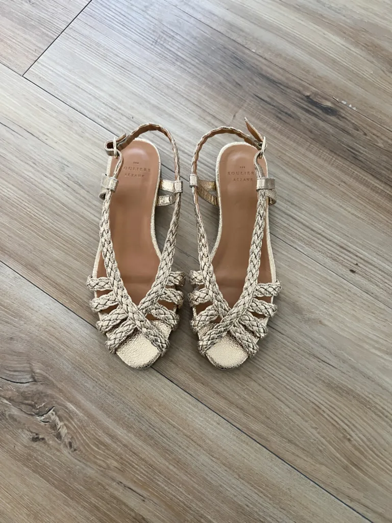 Gold sandals sitting on a floor.