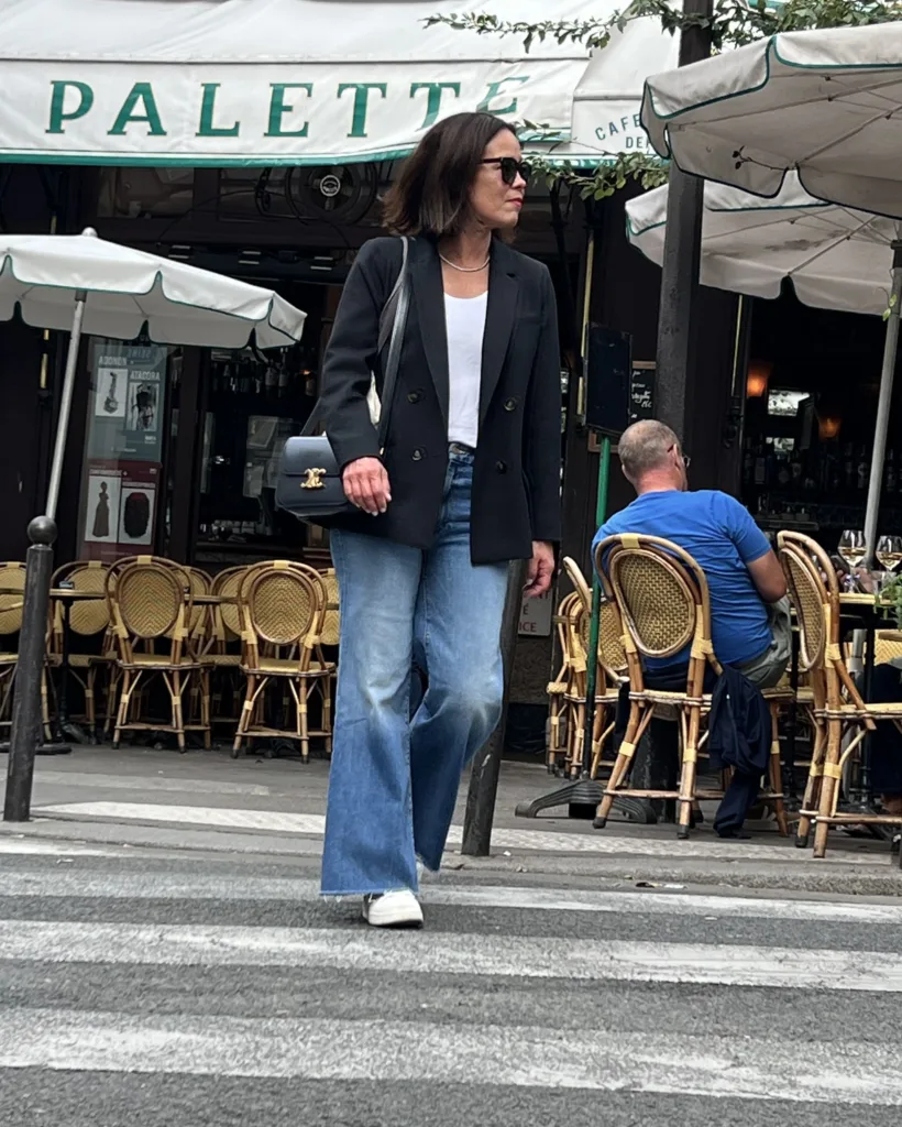 Woman walking wearing blue denim and black blazer across street in Paris | A Guide To Sézane Sizing