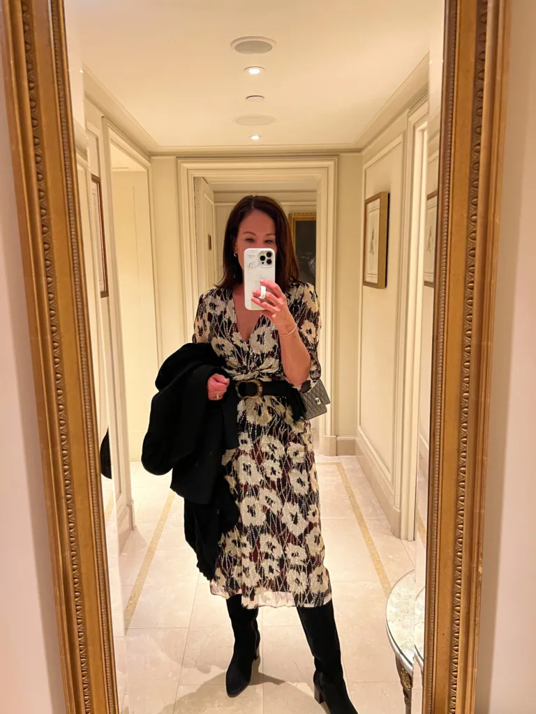 Woman looking into mirror wearing dress and boots.