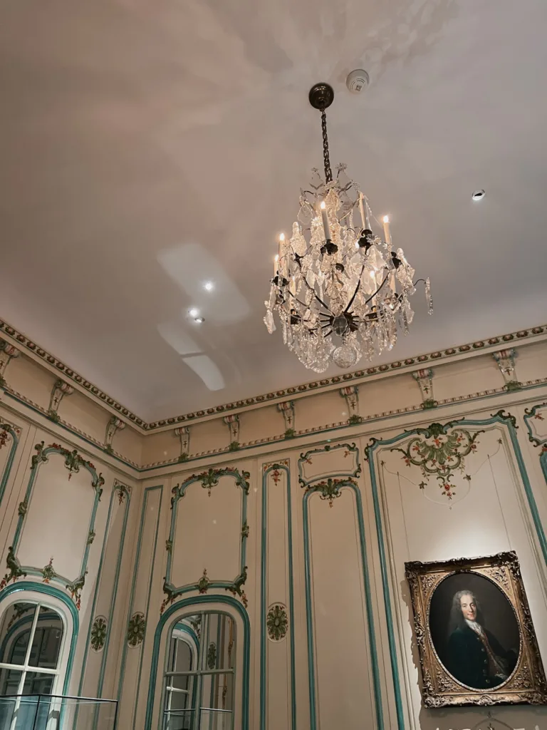Chandelier hanging from ceiling with green crown moulding, museum in Paris for French Fridays.