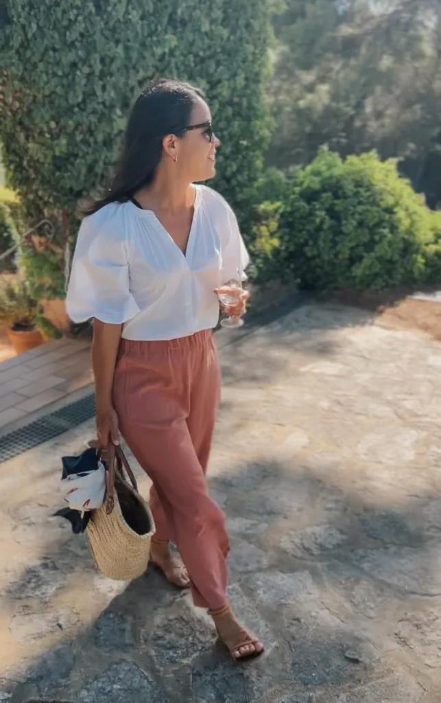 Lady wearing pink pants and white top walking with wine glass.