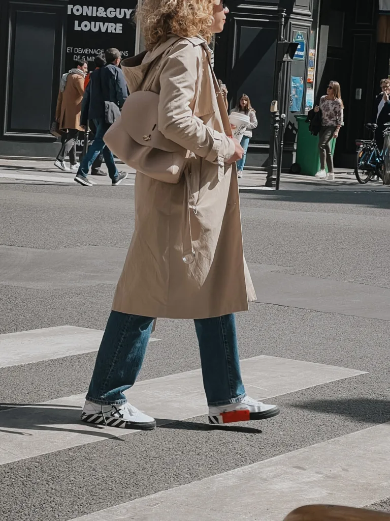 Lady wearing trench coat with sneakers walking in Paris.