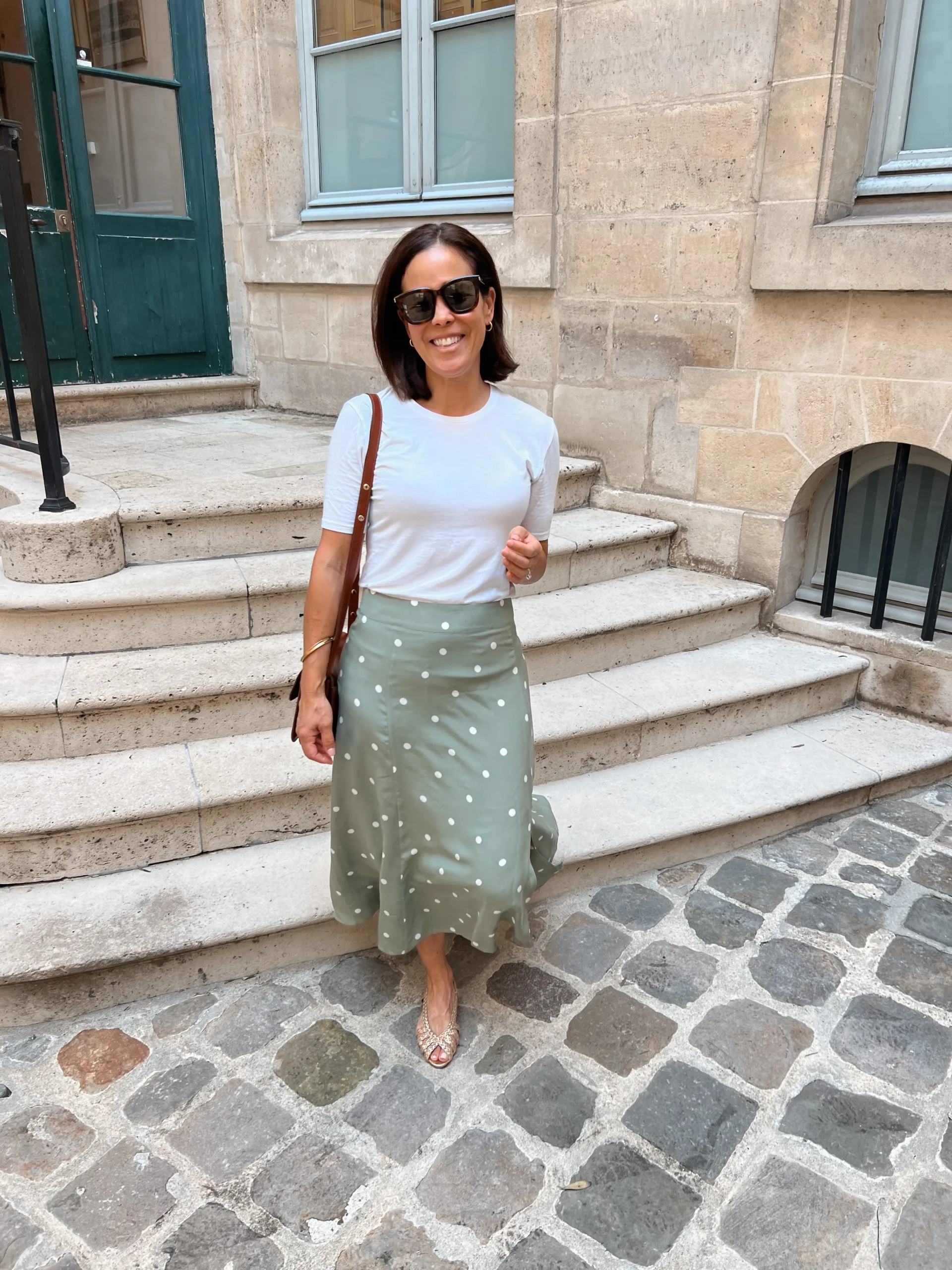 Woman wearing polka dot skirt with white tee and sandals. 