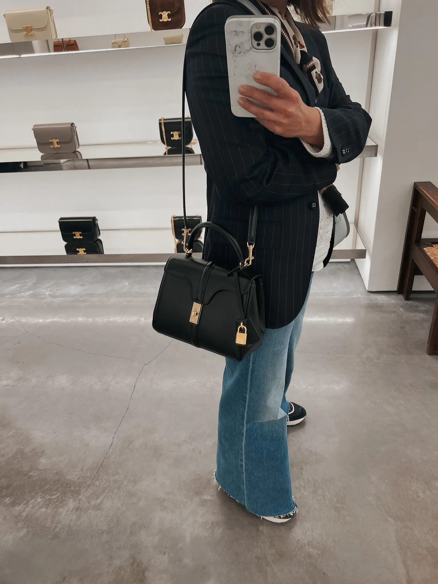 Woman wearing navy blazer, jeans, and holding black purse.
